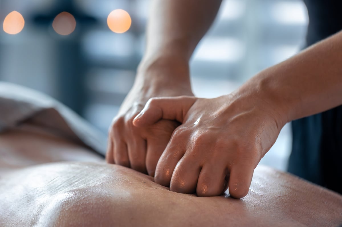 Two hands pressing on an oiled back during massage treatment