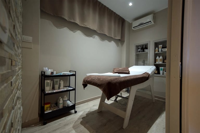 Professional massage therapy room with treatment table, shelving unit, white walls, and warm lighting