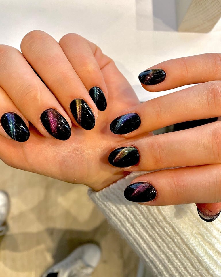 Close-up of manicured nails with black gel polish featuring holographic and glitter accents on all ten fingers