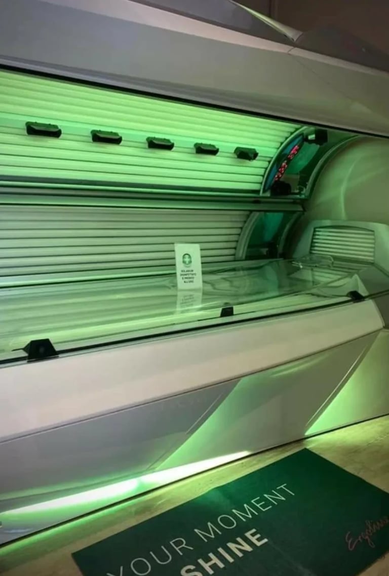 Interior view of a green tanning bed with horizontal UV lamps and illuminated green accents