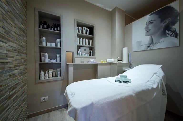 Modern spa treatment room with white massage bed, built-in shelving with skincare products, and accent wall tiling